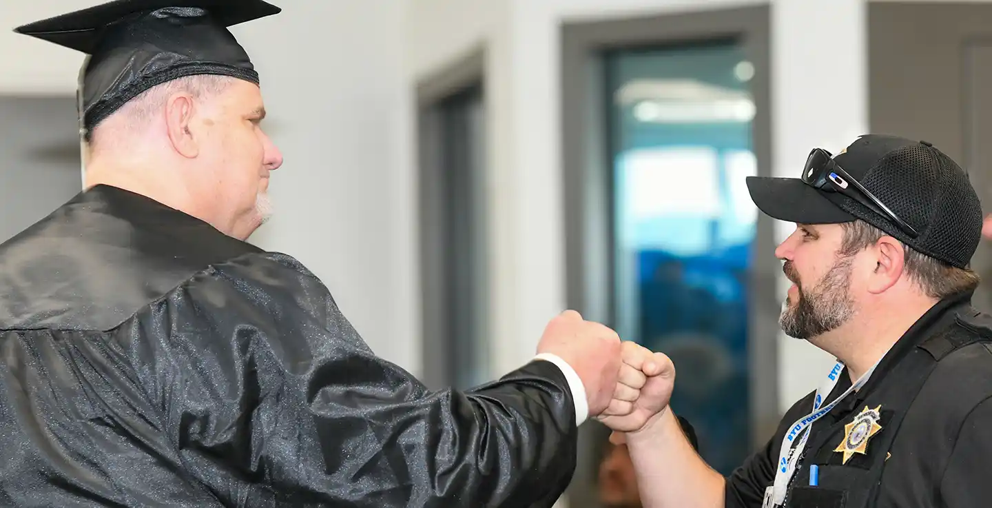 Incarcerated SLCC graduate doing a fist bump with corrections officer